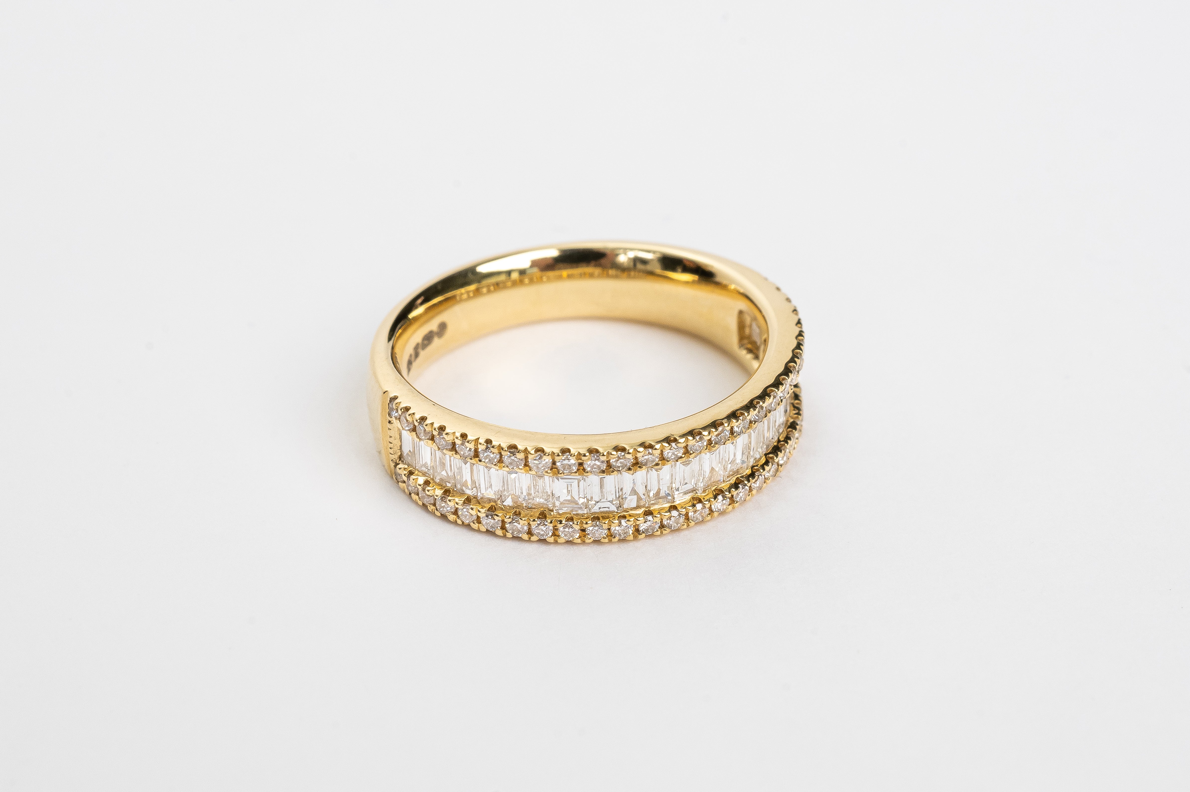 This baguette diamond ring is a showstopper! This new design is absolutely incredible. The baguette diamonds are set side by side to create sparkle from all angles. This triple row design has on both sides a row of round brilliant diamonds the close in the baguettes.   18kt yellow gold