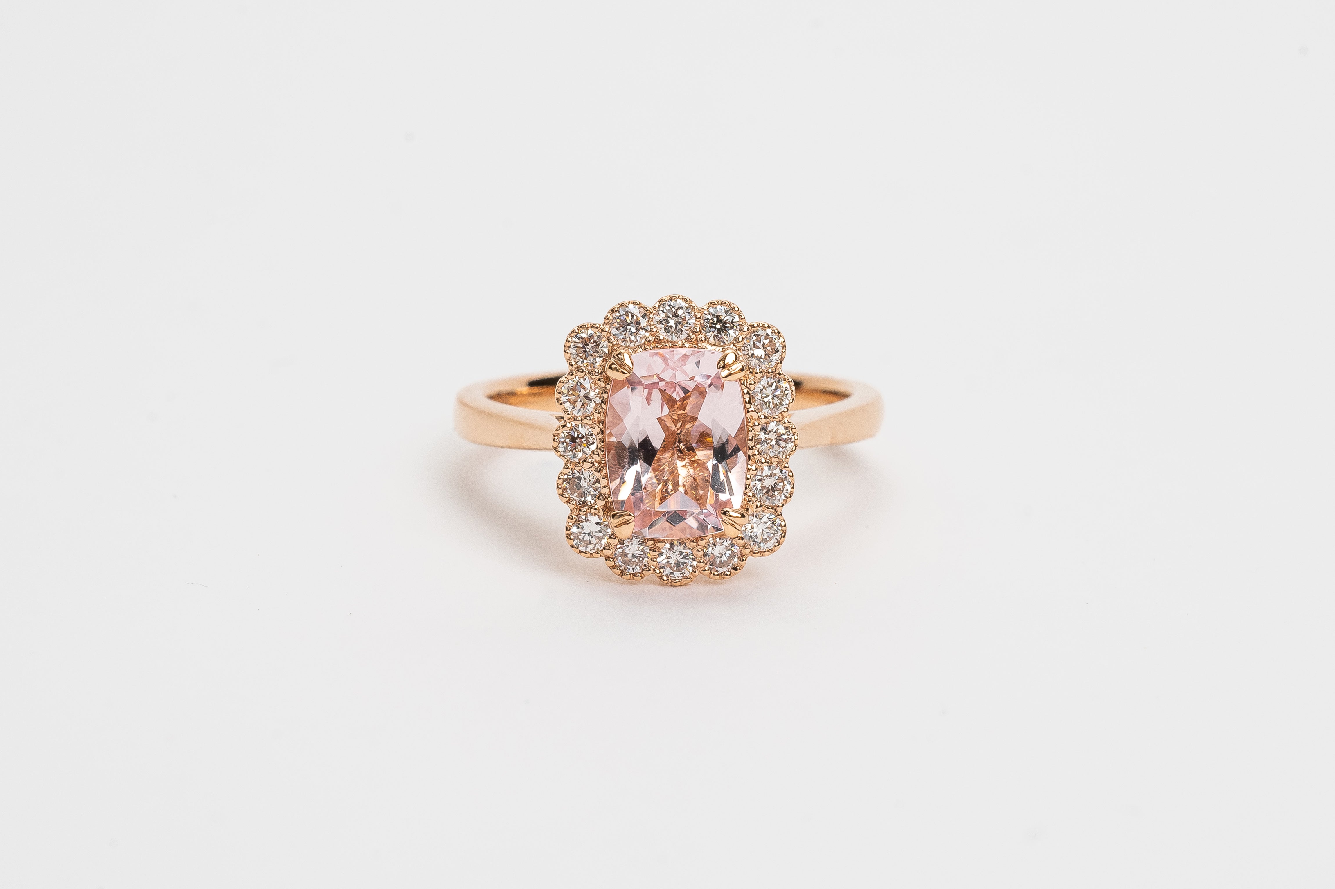 What a beautiful ring! The Morganite is cut in a cushion shape and surrounded by diamond halo of round brilliant diamonds. The soft peachy pink color of the stone matches so beautifully with the rose metal color of the ring.   18kt rose gold