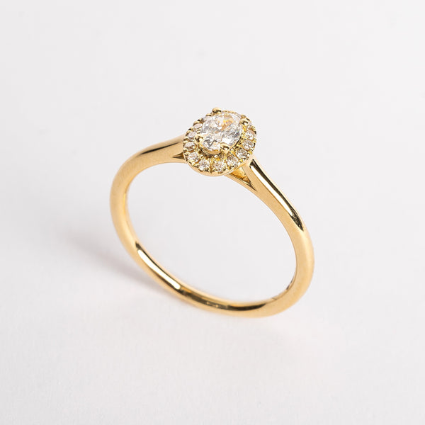 This is your engagement ring. This yellow golden ring is set with a brilliant diamond surrounded by a diamond halo. It looks perfect in its simplicity yet the halo makes the stone look more big.