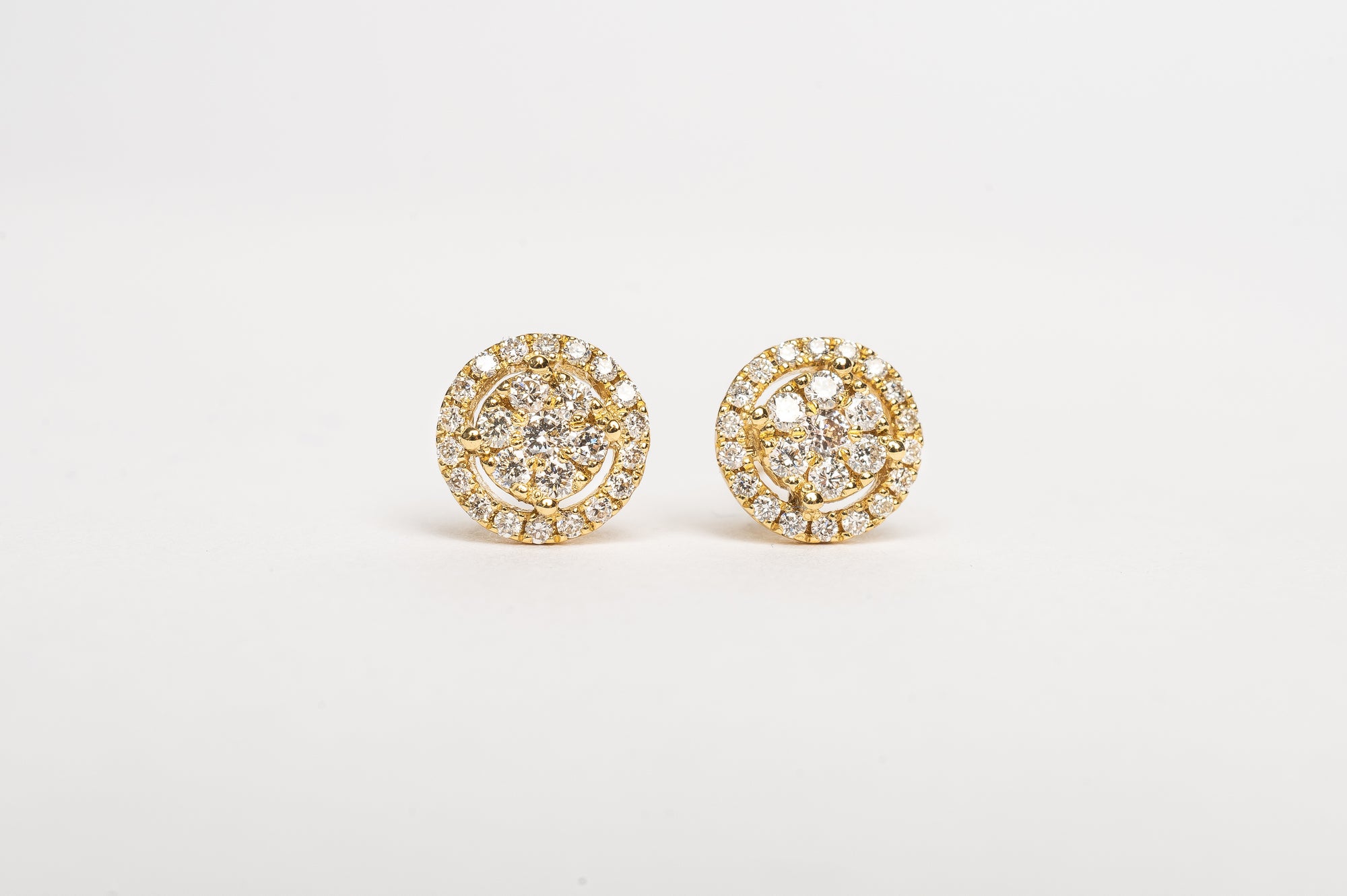 Timeless and modern, you will fall in love with these stunners. A beautiful round brilliant diamond in the center with smaller diamonds set in a halo. They are perfect for any ear.  18kt yellow gold Total diameter of the earring 5.6mm 3mm x 2 diamond center stone Center stone set with four claws Total dia